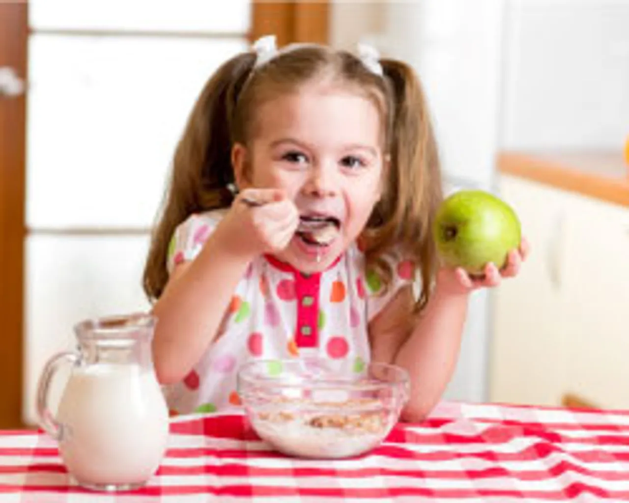 Little girl eating cereal and holding a green apple